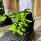 Rombai neoninių žalių batų raištelių detalė ant juodų sportbačių